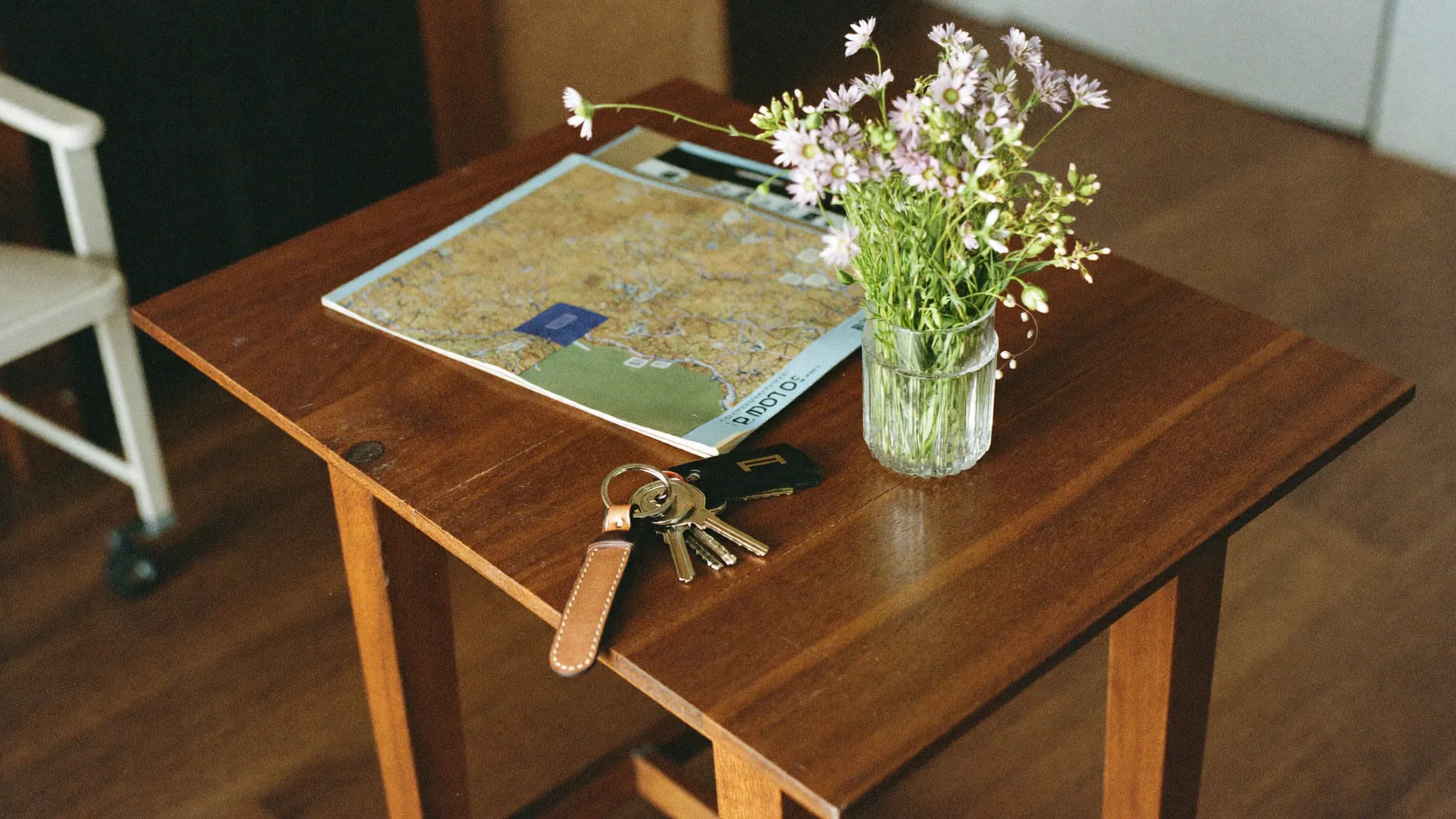 Kleiner Holztisch im Eingangsbereich der Ferienwohnung mit Schlüsseln, Landkarte und Wildblumen