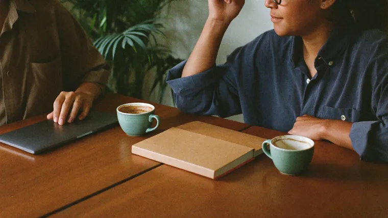 Unternehmerin und Webberater sitzen mit Kaffee am Holztisch und besprechen ihre Inhalte