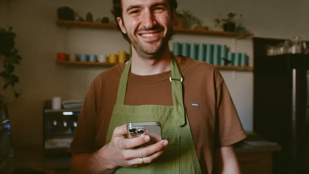 Café-Inhaber steht lächelnd mit Smartphone in seinem Laden