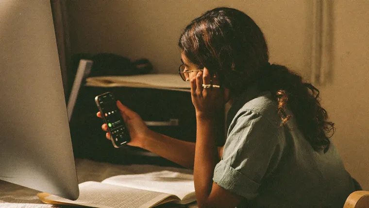 Unternehmerin sitzt nachdenklich mit dem Smartphone am Schreibtisch