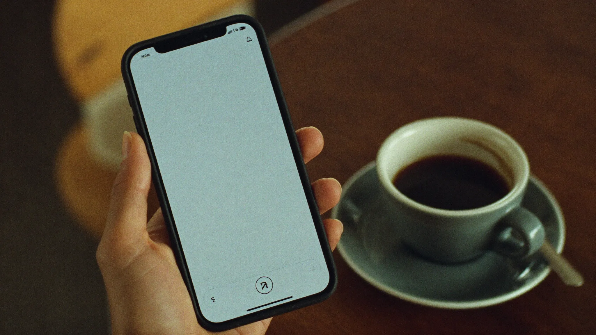 Hand hält ein Smartphone mit leerem Bildschirm, daneben ein kalt werdender Kaffee