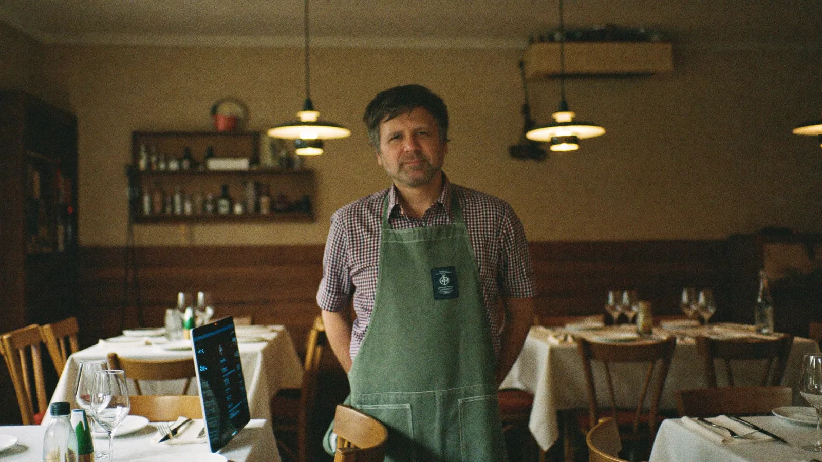 Restaurantinhaber steht in seinem gemütlichen, warm beleuchteten Gastraum
