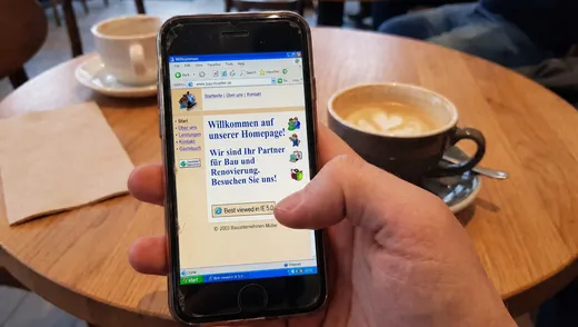 Hand hält ein Smartphone, auf dem eine alte Webseite winzig und unleserlich dargestellt ist